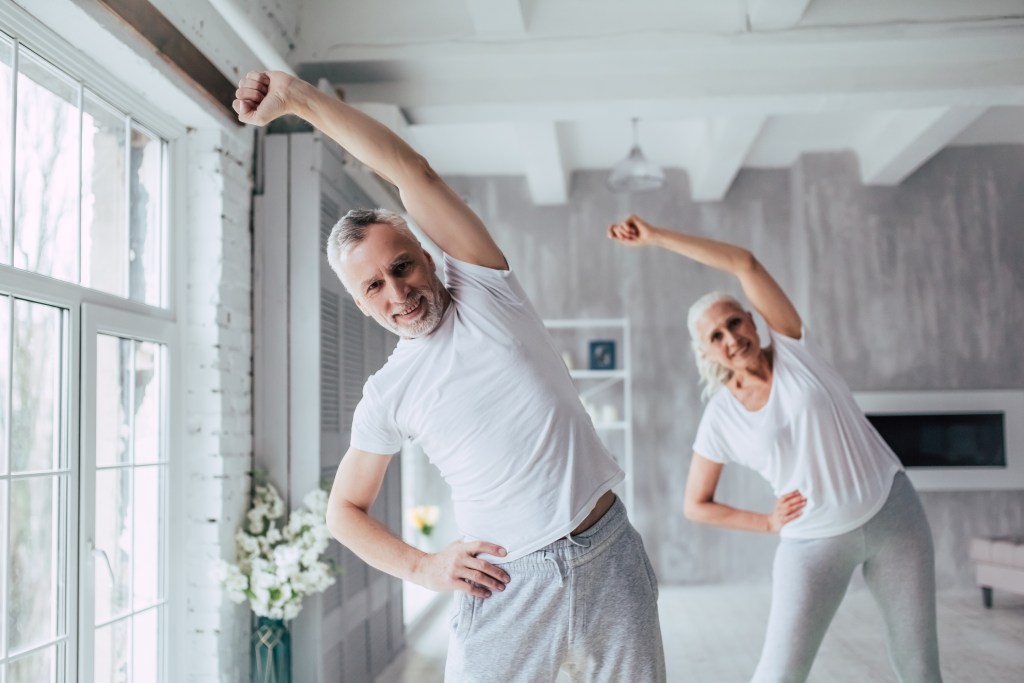 Un homme et une femme dans la cinquantaine faisant un étirement latéral debout.